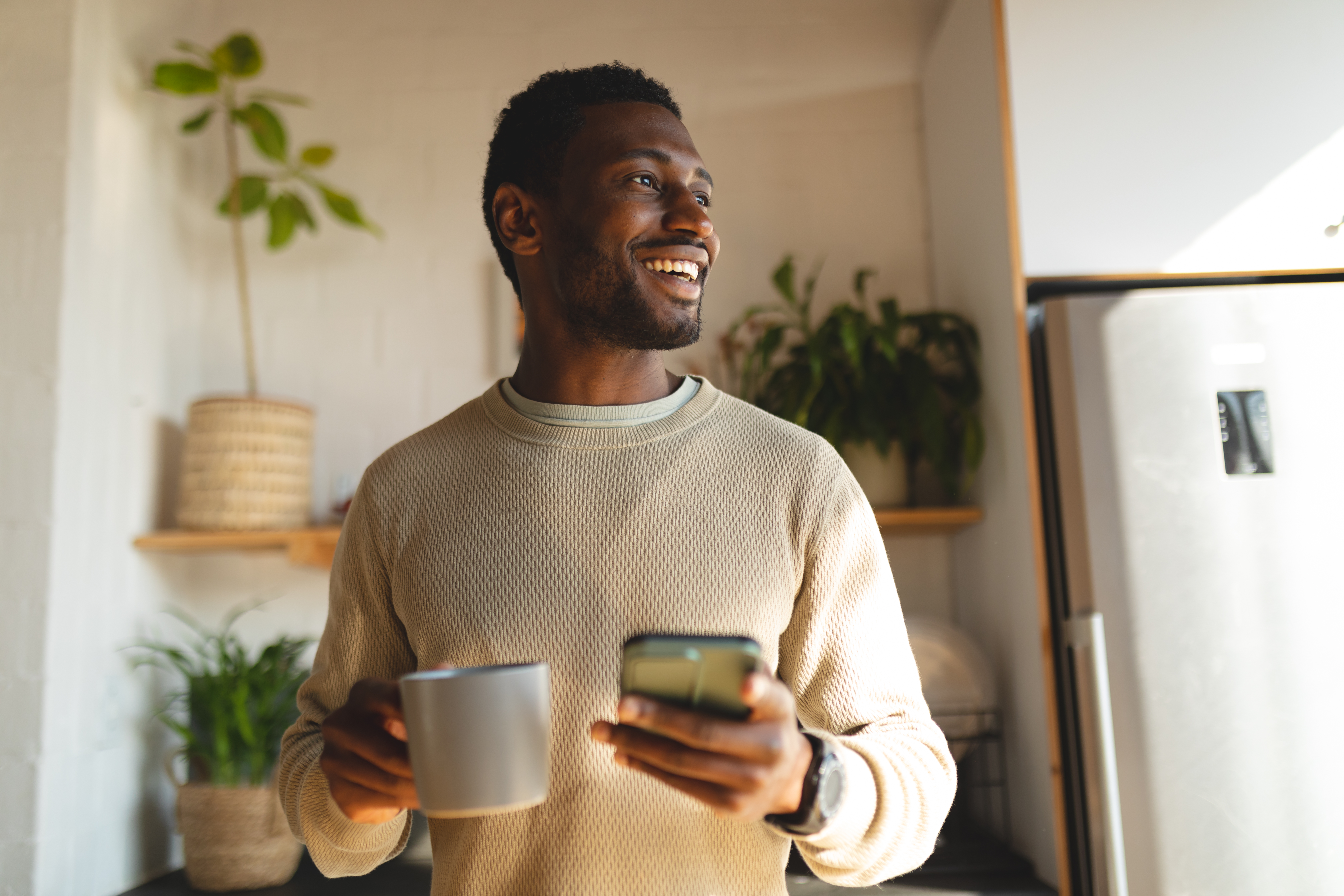 happy-african-american-man-using-smartphone-and-drinking-coffee-in-kitchen.jpg